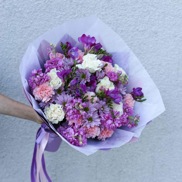 Hand-tied bouquet of purple, pink, and white flowers wrapped in lavender paper