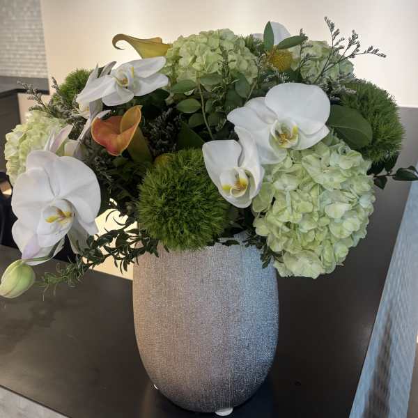 White orchids and pale green hydrangeas in a silver vase