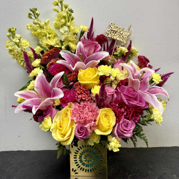 Bright mixed flower arrangement in a gold vase with a Happy Birthday topper
