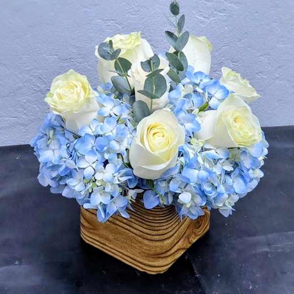 White roses and blue hydrangeas in a wooden basket
