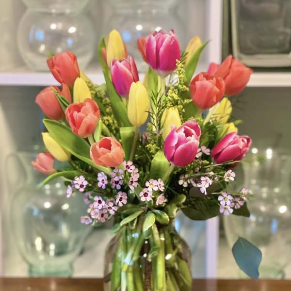 Mixed tulips in pink, coral, and yellow arranged in a glass vase