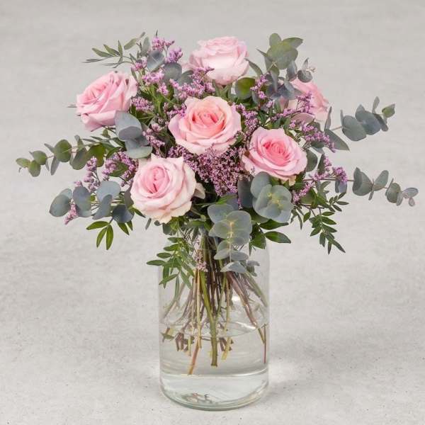 Pink roses in a clear glass vase with purple filler and eucalyptus