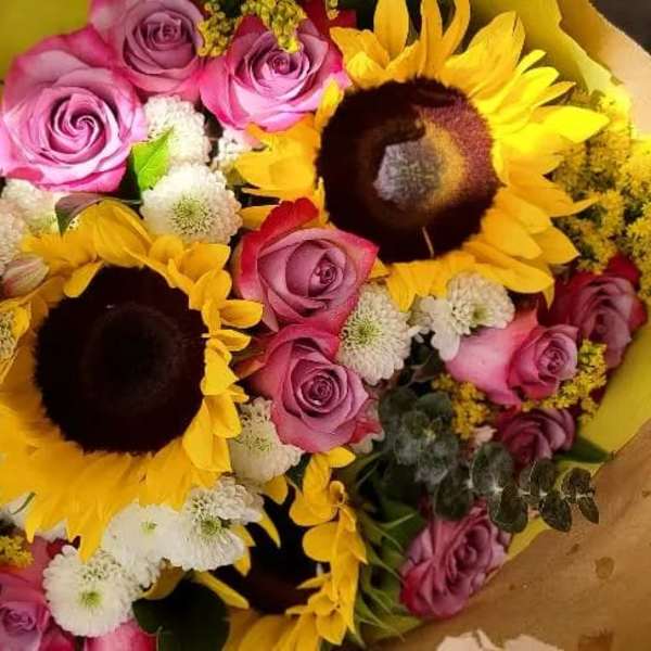 Bouquet of pink roses, sunflowers, and white pom flowers wrapped in yellow paper