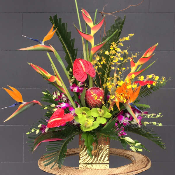 Tropical floral arrangement with birds of paradise, orchids, anthuriums, and protea in a gold vase