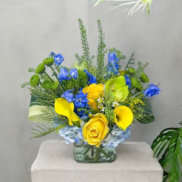 Blue and yellow floral arrangement in a square glass vase