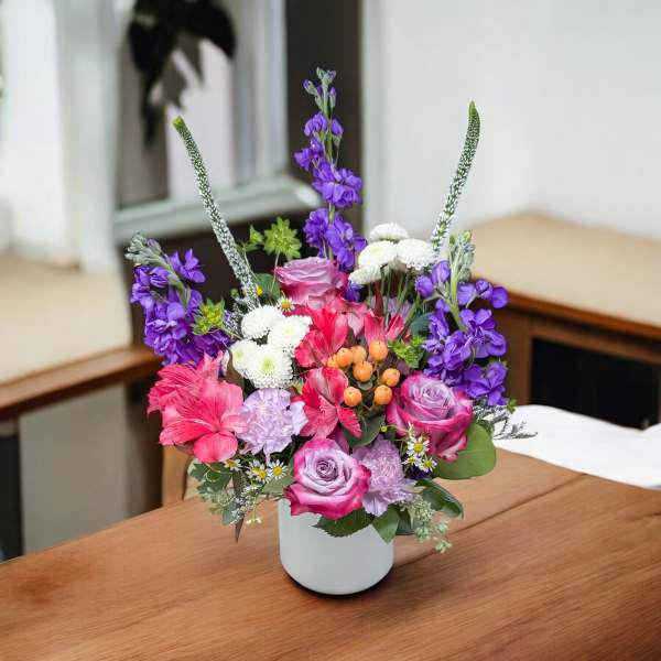 Mixed pink, purple, and white flowers arranged in a white vase