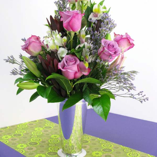 Pink roses and lilies arranged in a tall glass vase