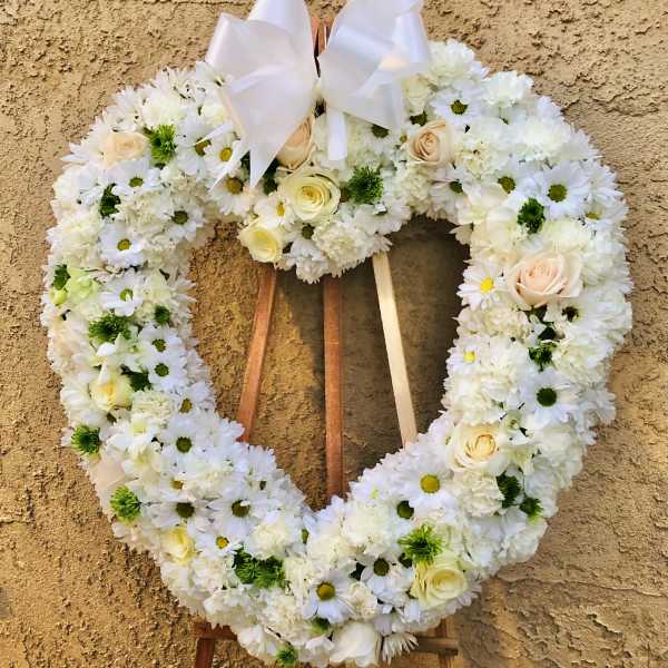 Heart-shaped white floral wreath with a ribbon bow on an easel