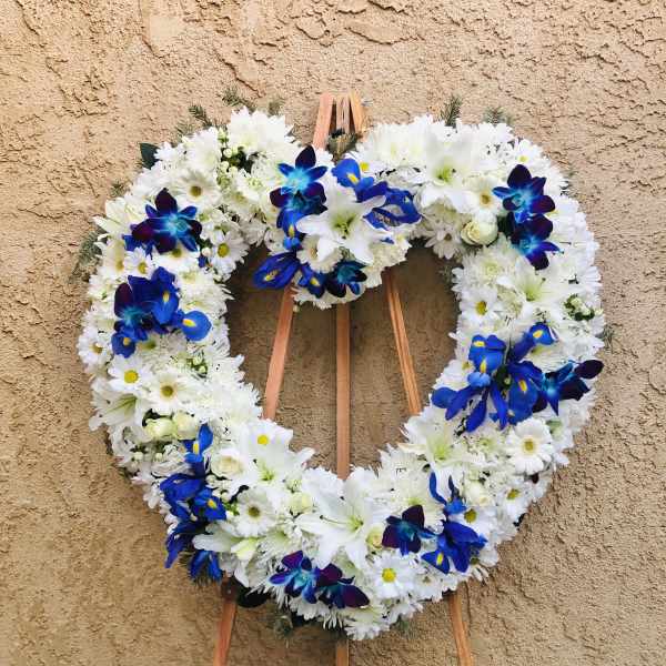 Heart-shaped white floral wreath with blue accent flowers on a wooden easel