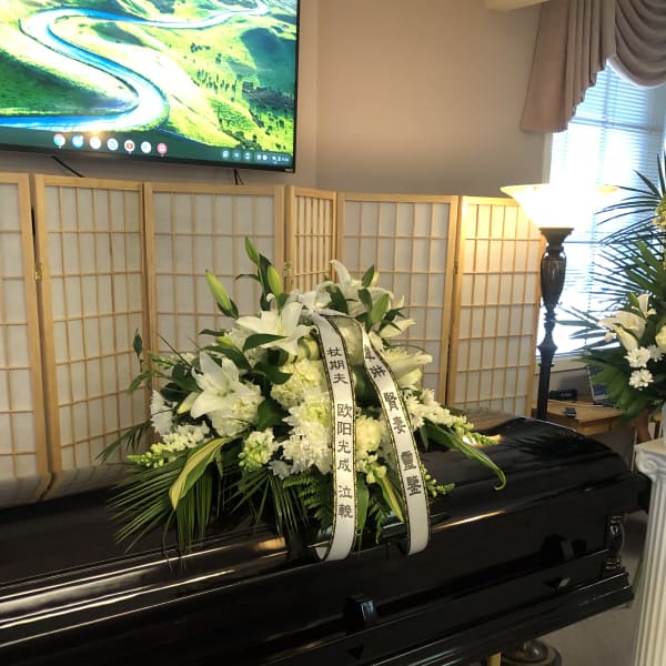 White funeral spray on a casket with ribbon streamers
