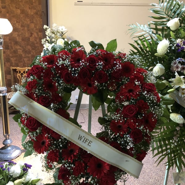 Heart-shaped red rose and gerbera wreath with a "WIFE" ribbon
