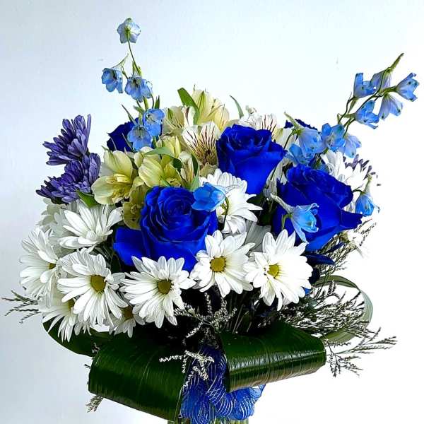 Blue roses and white daisies in a glass vase with ribbon