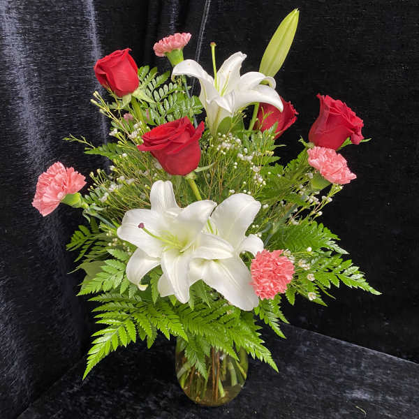 Bouquet of red roses, white lilies, and pink carnations in a glass vase