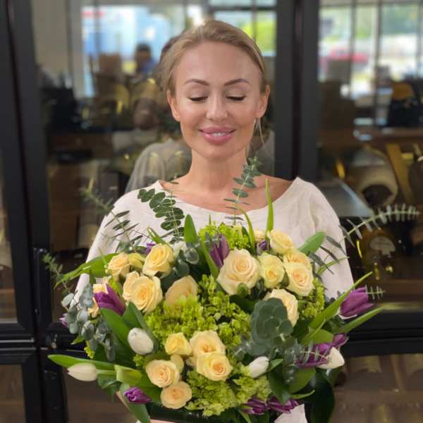 Woman holding a bouquet of pale yellow roses and purple tulips in a glass vase