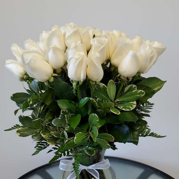 White roses arranged in a glass vase with a white ribbon