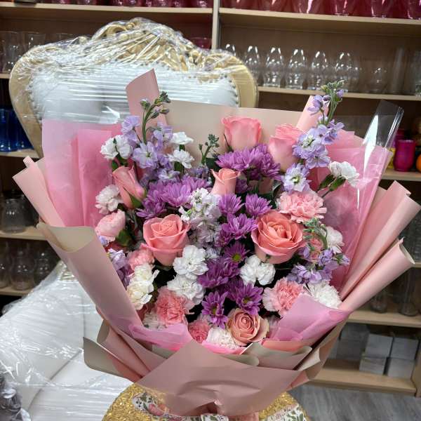 Hand-tied bouquet of pink roses, purple mums, and white and pink carnations wrapped in pink paper