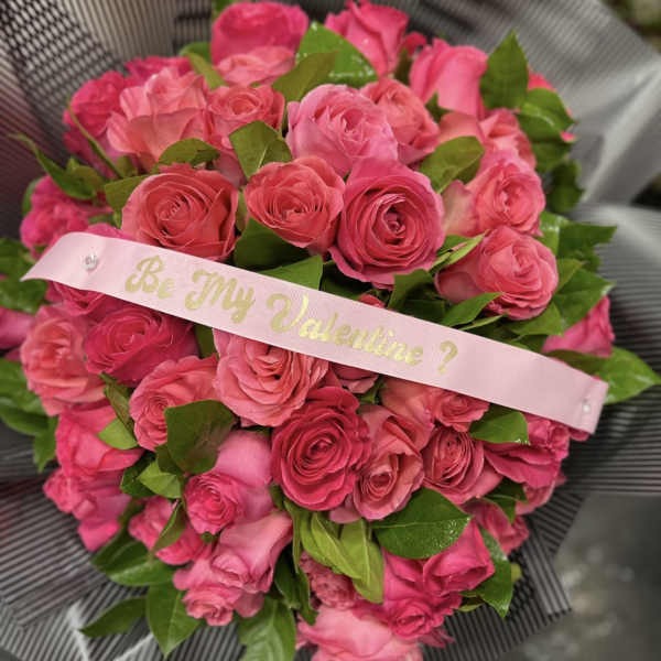 Bouquet of pink roses with a pink ribbon reading "Be My Valentine?"
