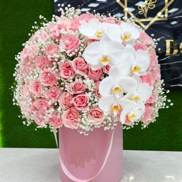 Pink roses and white orchids arranged in a pink hatbox