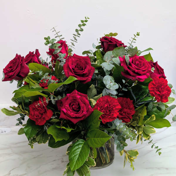 Red roses and carnations in a glass vase with mixed greenery