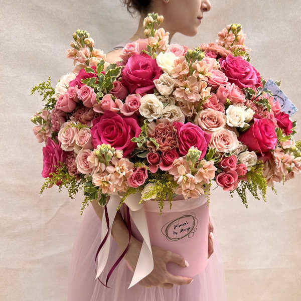 Large pink hatbox arrangement of hot pink and blush roses and mixed flowers held by a woman.