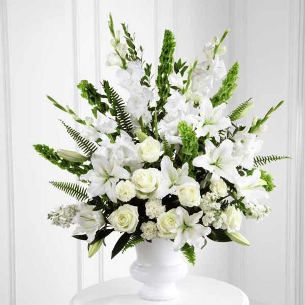 Tall white arrangement of lilies, roses, and carnations in a white pedestal vase