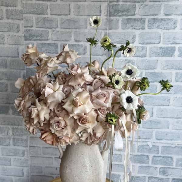 Blush roses in a white vase with white anemones and ribbon accents