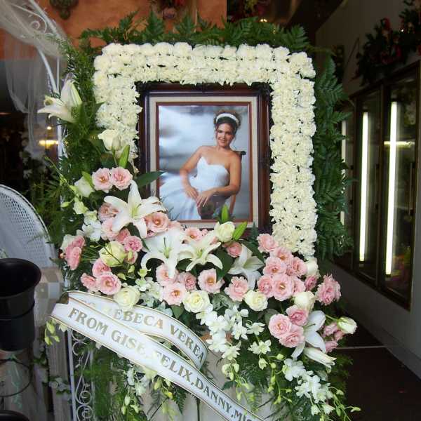 Funeral floral tribute with a framed portrait, white lilies, and pink roses
