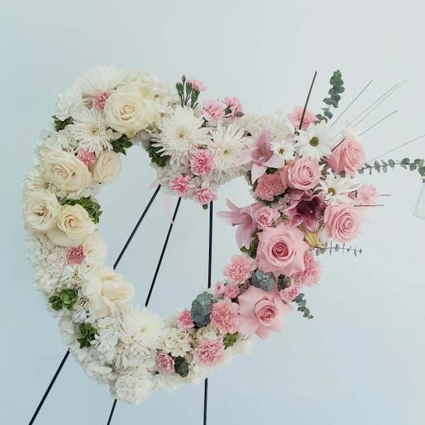 Heart-shaped floral wreath with white and pink flowers on a stand