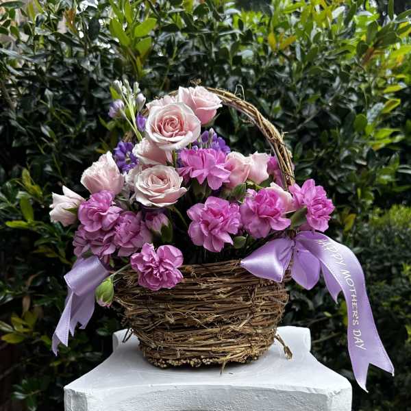 Pink roses and carnations in a wicker basket with lavender ribbons