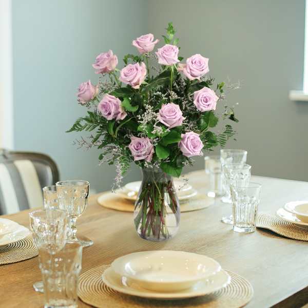Lavender rose bouquet in a clear glass vase on a set dining table