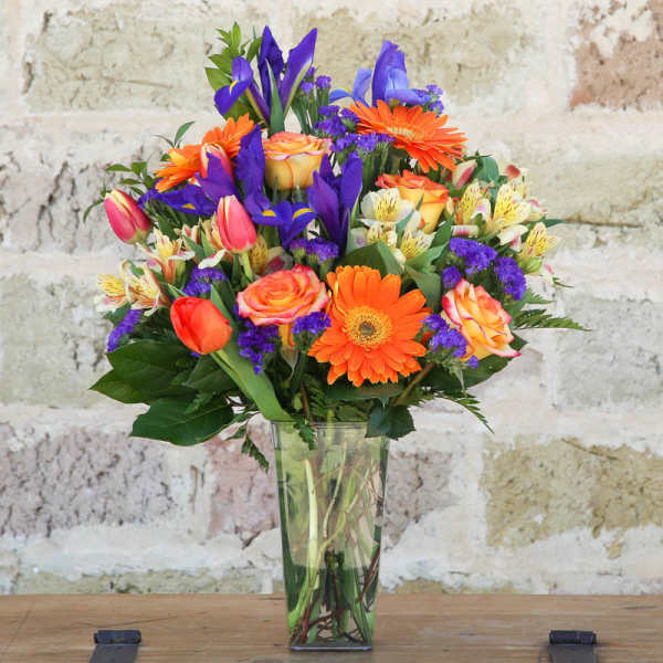 Mixed bouquet of orange, purple, pink, and yellow flowers in a clear glass vase