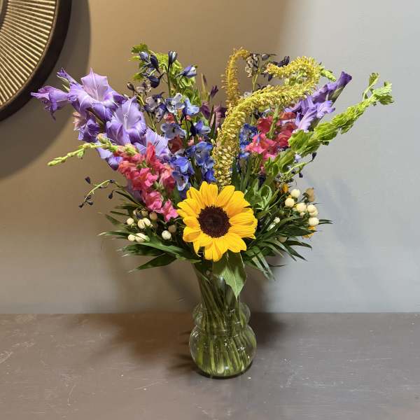 Mixed bouquet with a sunflower and purple, pink, and blue flowers in a glass vase
