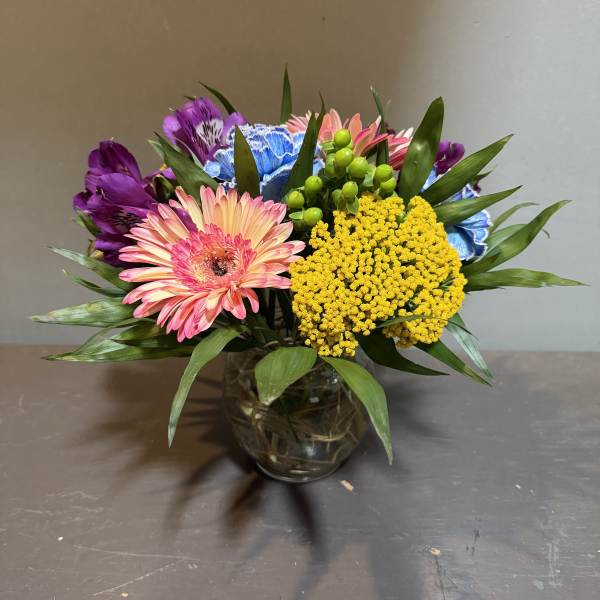 Mixed bouquet of pink gerbera daisies, purple alstroemeria, and yellow filler in a glass vase