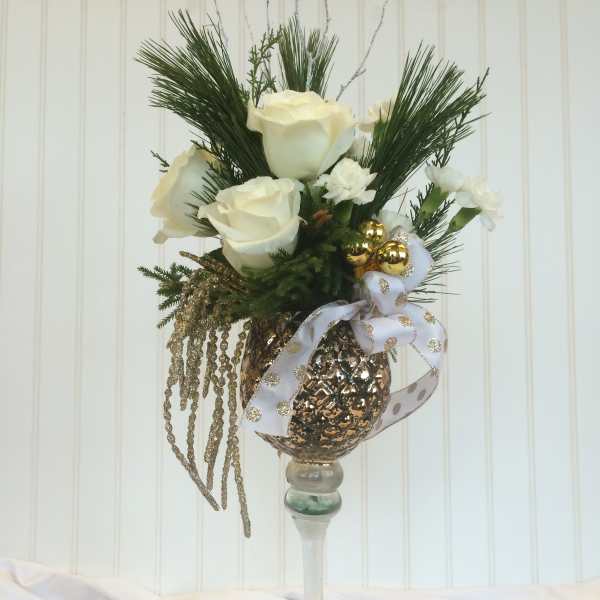 White roses arranged in a tall glass vase with gold ornaments and ribbon