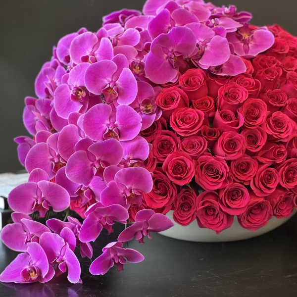 Pink orchids and red roses arranged in a low white bowl