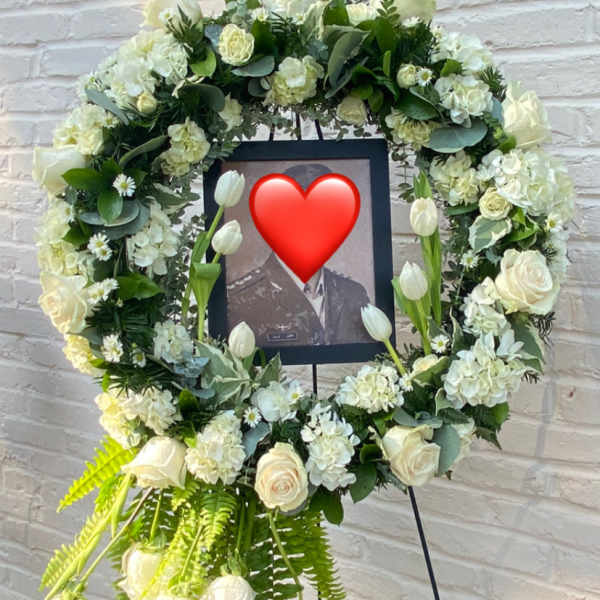 White floral funeral wreath on an easel with a framed photo in the center