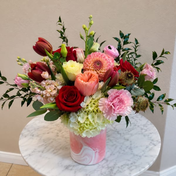 Mixed bouquet of roses, tulips, dahlias, and carnations in a pink vase