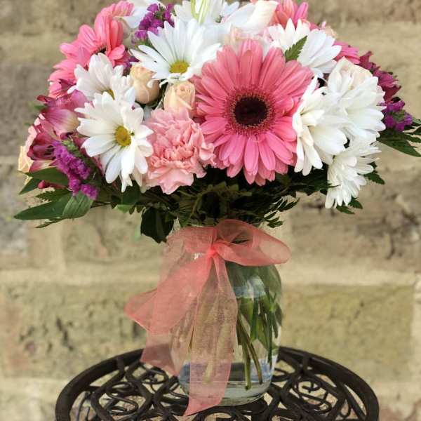 Pink and white daisy bouquet in a glass vase with a pink ribbon