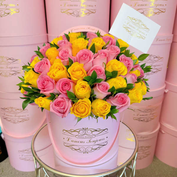 Round pink hatbox filled with pink and yellow roses and a card on a mirrored table