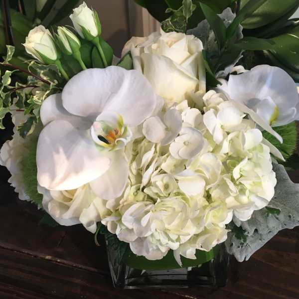 White roses, hydrangeas, and calla lilies arranged in a glass vase