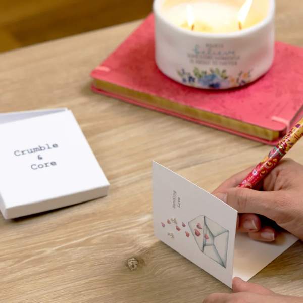 Candle on a pink book beside a greeting card being written