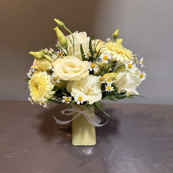 Cream and yellow bouquet in a small vase with a sheer ribbon