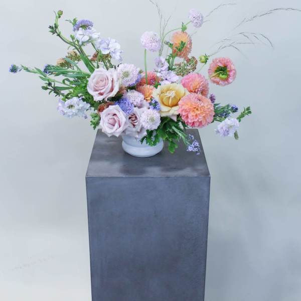 Pastel mixed flower arrangement in a white vase on a pedestal