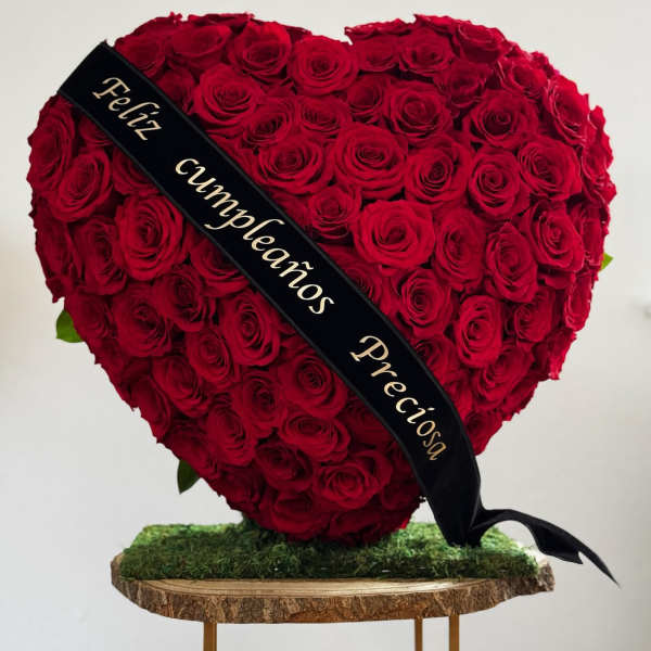 Heart-shaped red rose arrangement with a black ribbon on a wood slab stand