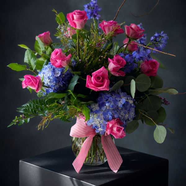 Pink roses and blue hydrangeas in a glass vase with a pink ribbon