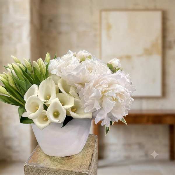 White floral arrangement with calla lilies and peonies in a white vase