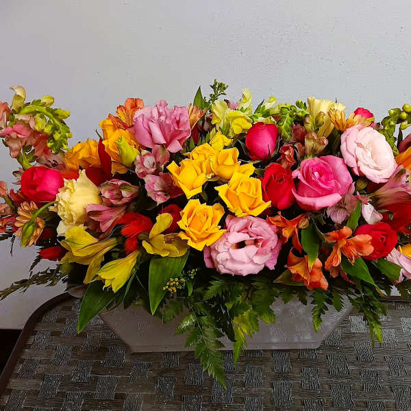 Long low arrangement of multicolored roses and alstroemeria in a rectangular container