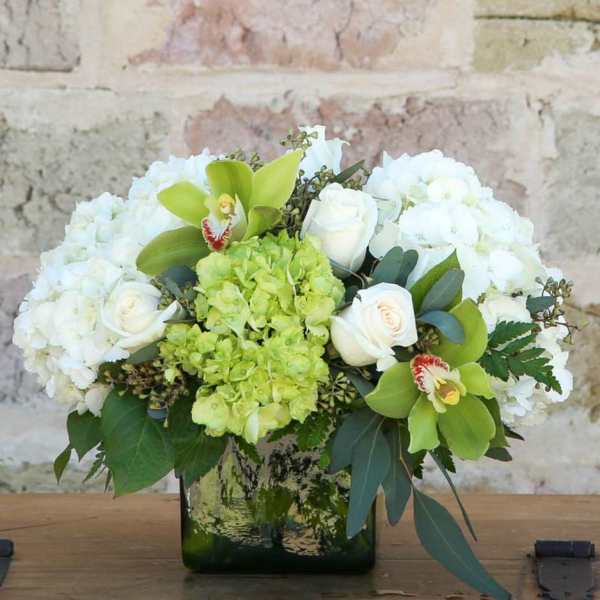White and green floral arrangement in a square glass vase