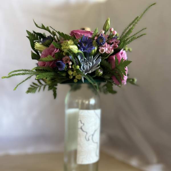 Colorful mixed bouquet with pink and blue flowers arranged in a tall glass bottle.