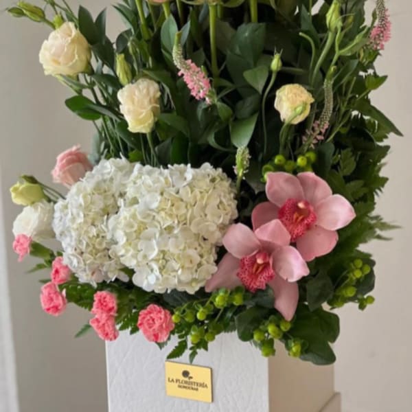 Pink roses, white hydrangea, and pink orchids arranged in a white box
